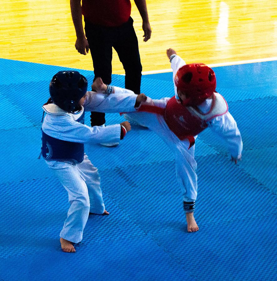 Un niño de careta roja lanza una patada a su rival de peto azul