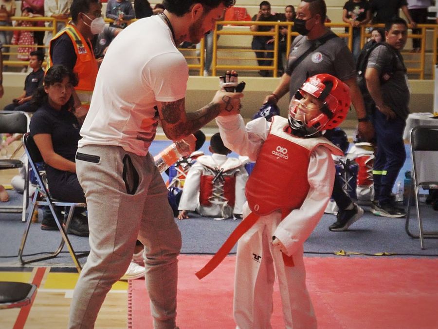 El entrenador choca la mano con un niño sonriente de careta y peto rojos