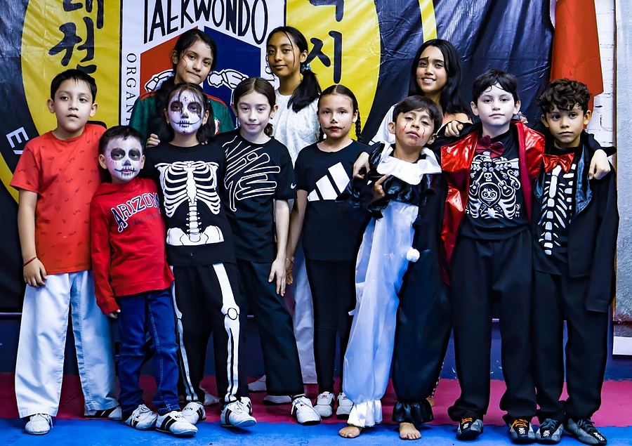 Alumnas y alumnos disfrazados y maquillados para Día de Muertos frente a la manta del club