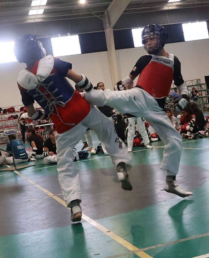 Un competidor de peto rojo conecta una patada en el peto de su rival