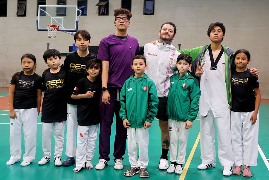 Alumnos con playeras REAL y chamarras de México posan con el entrenador en un gimnasio
